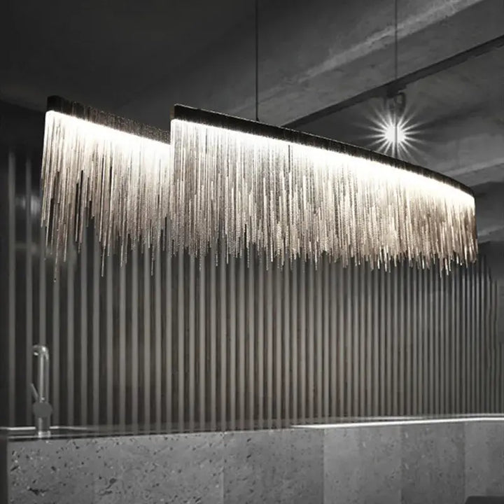 Linear chandelier with long tassels illuminating a modern dining room, featuring sleek design and warm glow.