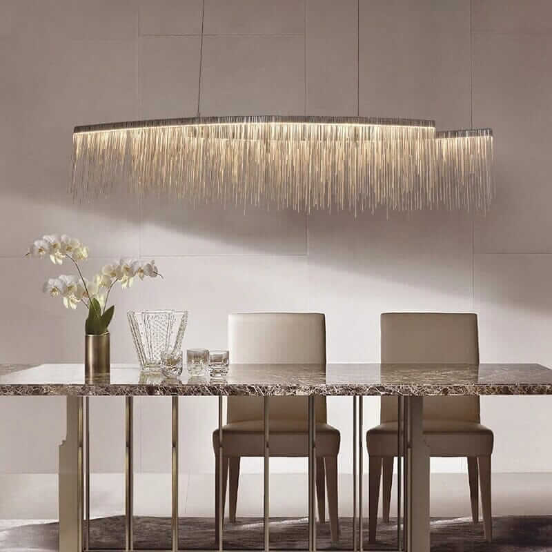Elegant linear chandelier with long tassels illuminating a modern dining room with sleek furniture.