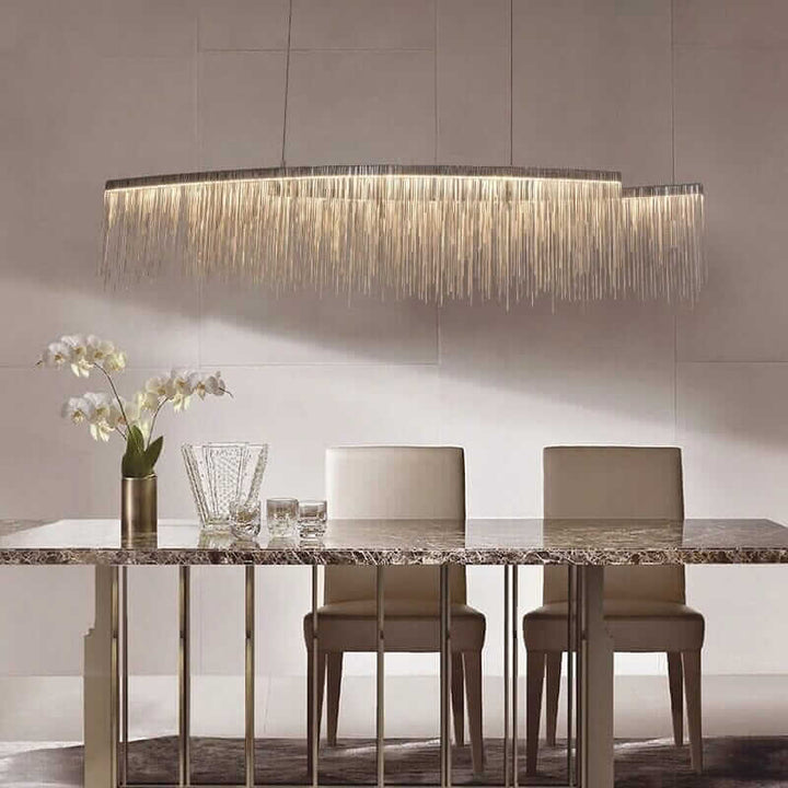 Elegant linear chandelier with long tassels illuminating a modern dining room with sleek furniture.