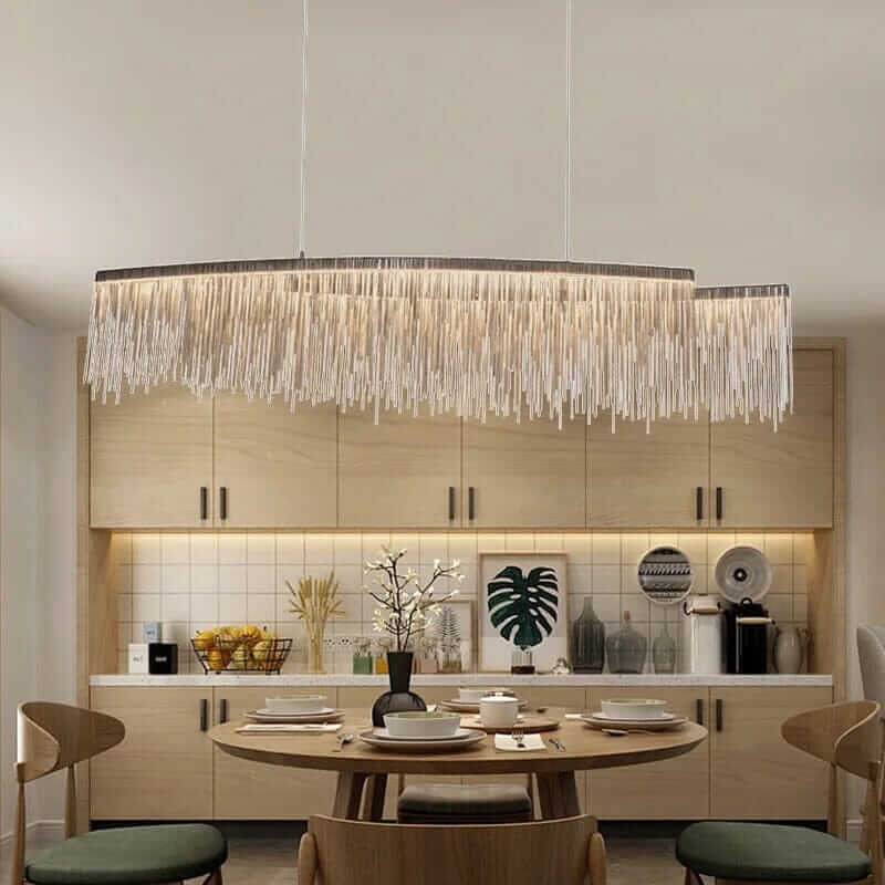 Linear chandelier with long tassel design illuminating a modern dining room with a wooden table and warm decor.