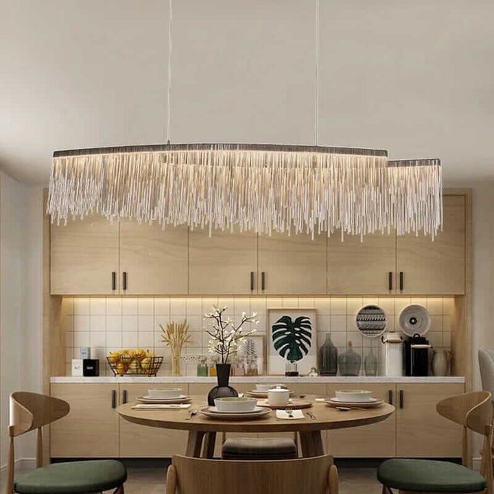 Linear chandelier with long tassel design illuminating a modern dining room with a wooden table and warm decor.