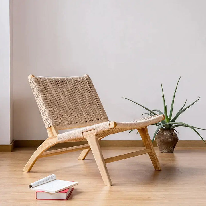 Wood lounge chair with rattan weaving, set in a minimalistic home interior with a plant and books.