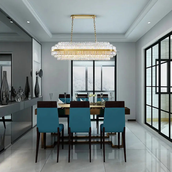 Elegant gold chandelier illuminating a modern dining room with stylish teal chairs and large windows.