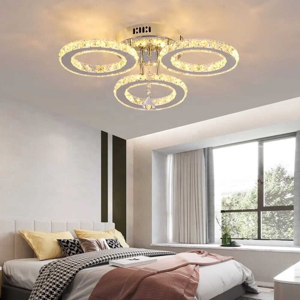Small crystal chandelier with three circular tiers illuminating a modern bedroom, adding elegance and glamour.