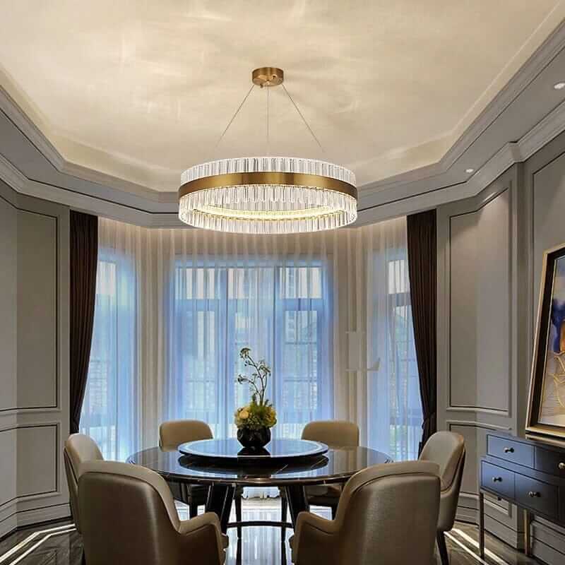 Elegant gold crystal chandelier illuminating a modern dining room with stylish decor and large windows.