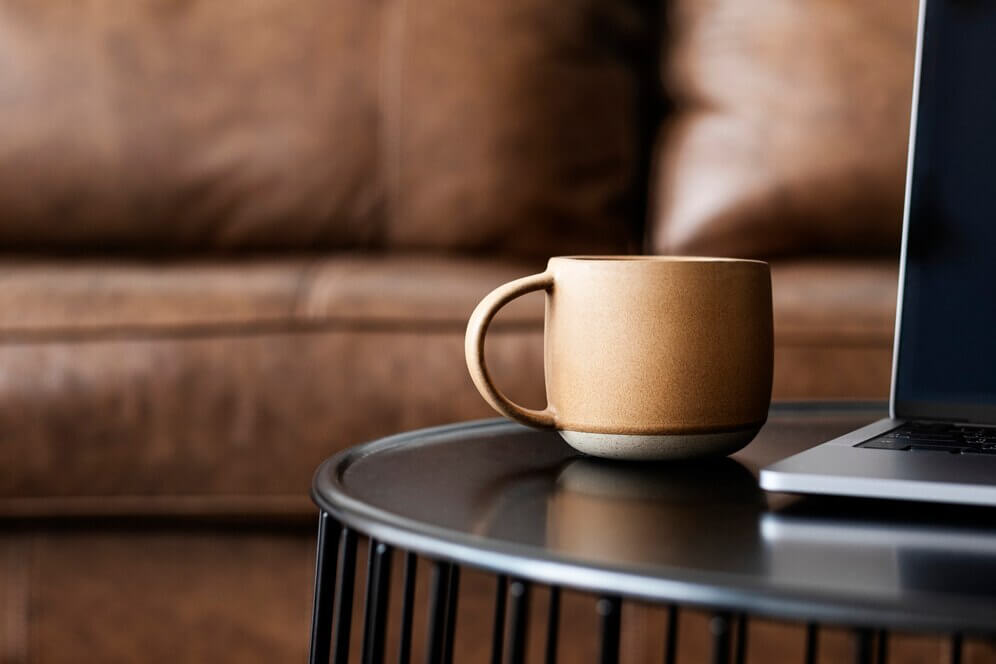 Coffee Tables with a brown mug and laptop on a stylish black table in a cozy living room setting.