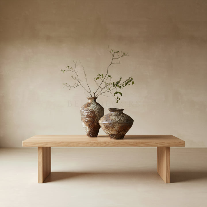 Two ceramic vases with branches on a wooden bench against a beige wall.