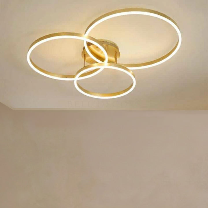 Ceiling light fixture with three circular gold rings on a plain background