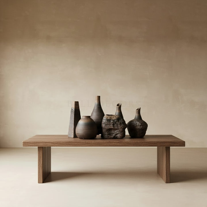 Set of five ceramic vases on a wooden bench against a beige wall.