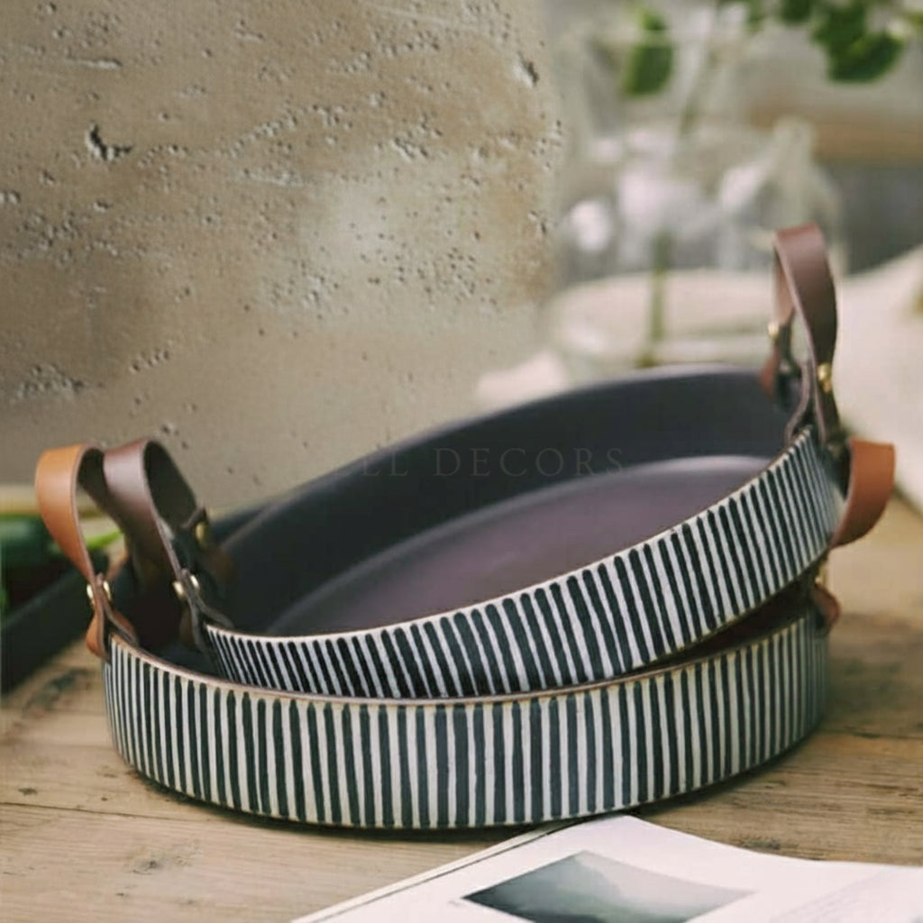 Set of ceramic trays with striped design and leather handles on a wooden surface.