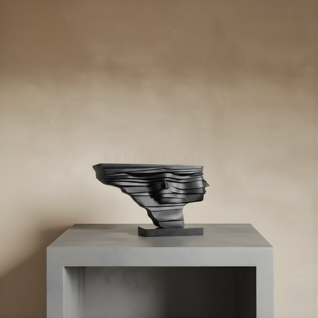 Black abstract sculpture on a gray pedestal against a beige wall