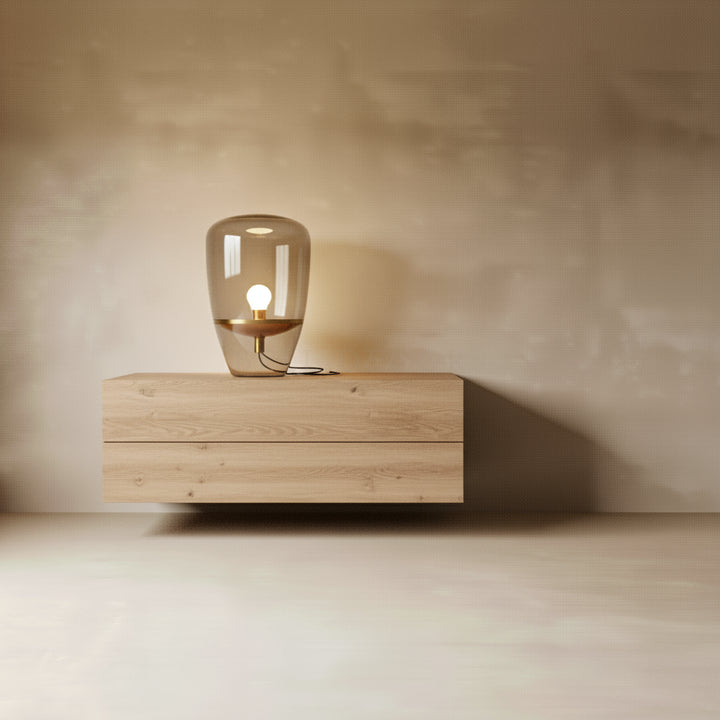 Wooden nightstand with a glass table lamp against a plain wall.
