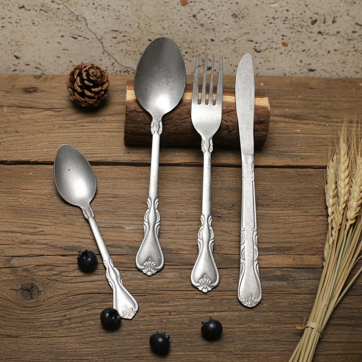 Set of silver cutlery including spoons, fork, and knife on a wooden surface with natural elements.