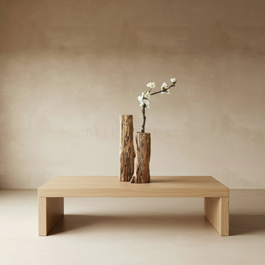 Wooden table with two wooden vases and a branch with white flowers against a beige wall.