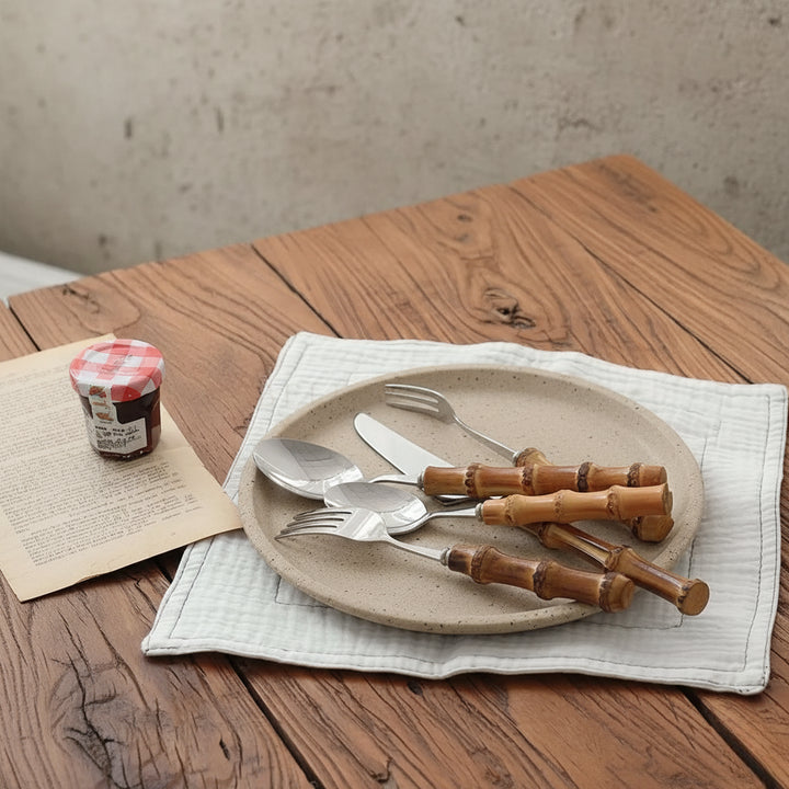 Set of cutlery with wooden handles on a plate with a jar of jam and paper on a wooden table.