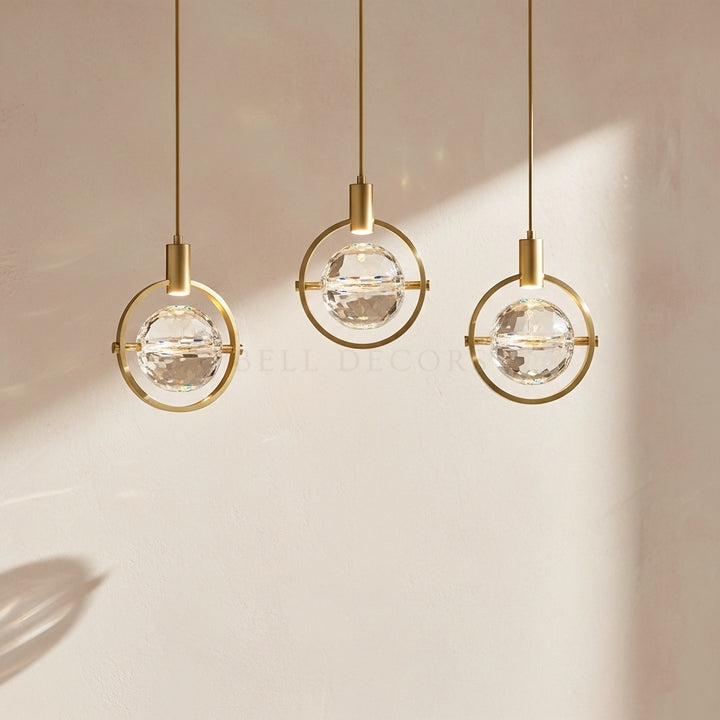 Three modern pendant lights with gold frames and clear glass globes on a neutral background.
